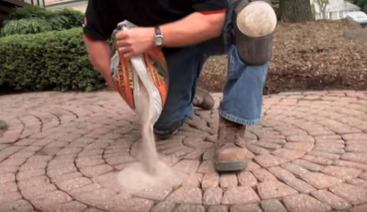 Professional paving company pours new paver sand between cracks of stones.